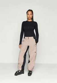 Μαύρο πουκάμισο με μακριά μανίκια, μπεζ παντελόνια χιονιού με ναυτικές πλευρικές ρίγες, με κλείσιμο από φερμουάρ και κουμπιά, που διαθέτει τσέπες με φερμουάρ και λογότυπο βουνού.