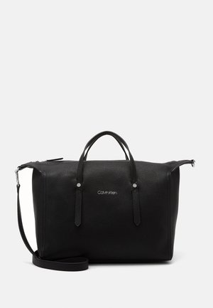 Czarna, teksturowana skórzana torba podróżna typu duffel z podwójnymi uchwytami, regulowanym paskiem na ramię oraz logo "Calvin Klein" na przednim środku.