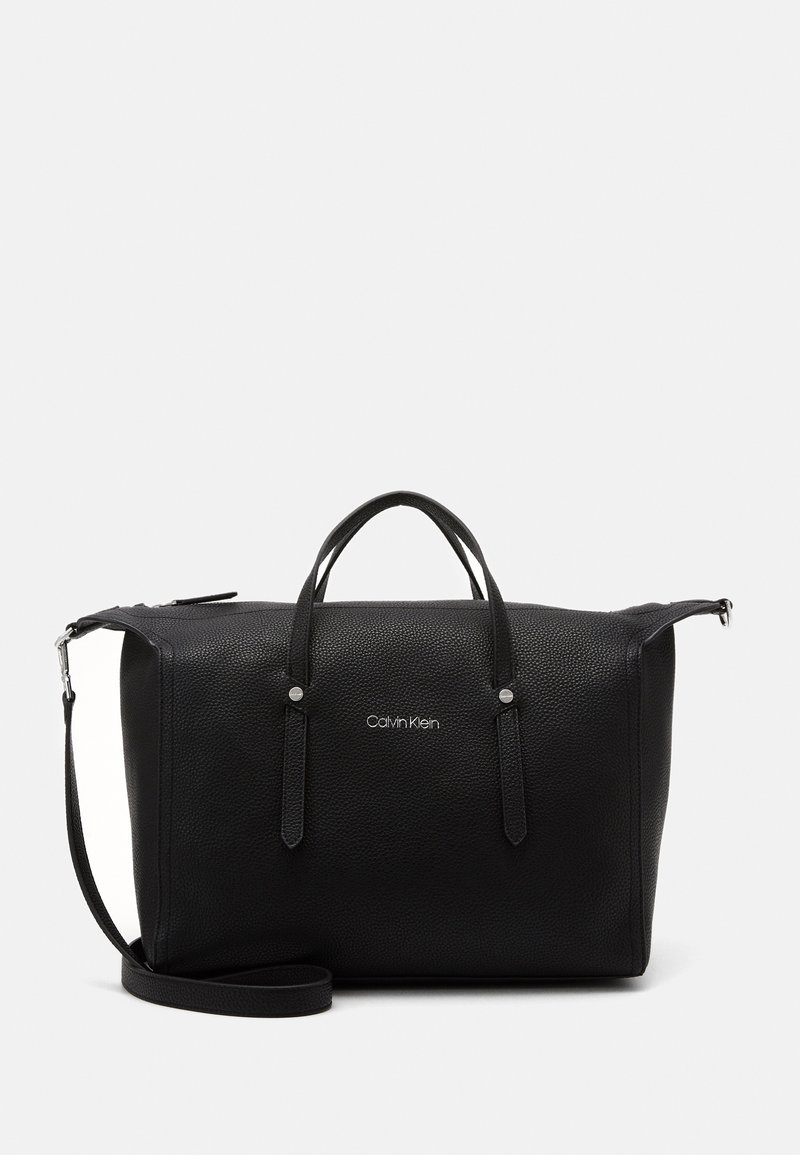Sac de voyage en cuir noir texturé avec doubles poignées, bandoulière réglable et logo "Calvin Klein" au centre avant.