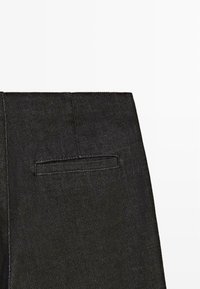 Pantalons en denim noir avec une finition texturée, dotés d'une poche arrière unique et d'une taille épurée. Design simple et moderne.
