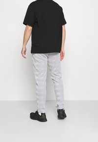 Schwarzes kurzärmliges Shirt, graue karierte Hose mit strukturiertem Muster und schwarze Sneaker, von hinten vor einem schlichten Hintergrund betrachtet.