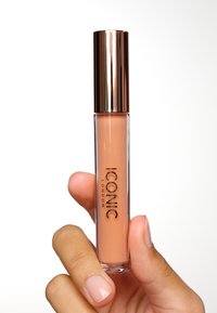 Transparent läppglans i en cylindrisk tub med ett roséguldlock. Formeln verkar krämig och har en naken färg. Märkesnamnet är synligt.