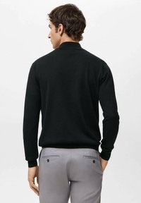 Musta neulottu pusero, jossa on tasainen kaulus ja pitkät hihat, yhdistetty harmaisiin housuihin, joissa on takataskut ja nappidetalji.