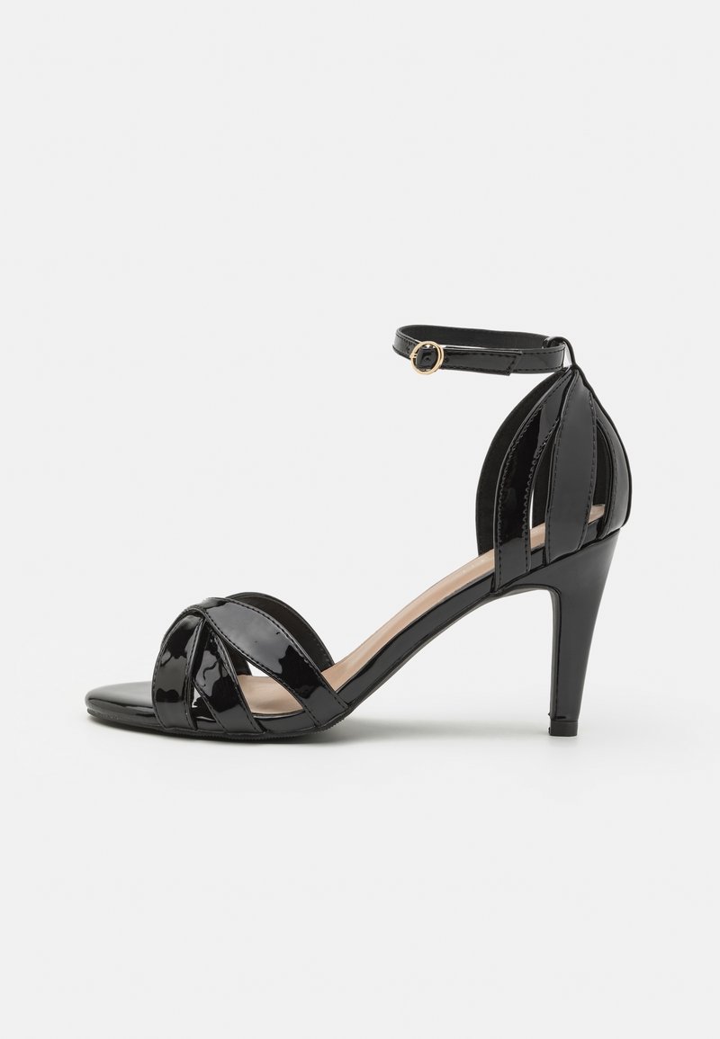 Sandale à talon haut en cuir verni noir avec bride à la cheville et boucle dorée, bout ouvert, avec des éléments décoratifs en forme de feuille à l’avant et au talon.