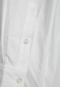 White long-sleeve shirt with a smooth cotton texture, featuring a button cuff with a round, pearlescent button and a geometric collar detail.