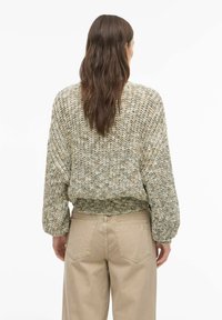Pull court en maille dans des tons beige et vert, présentant un motif texturé et un ourlet élastique. Associé à un pantalon beige taille haute.
