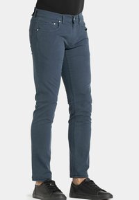 Jeans attillati blu scuro con cinque tasche, accessori in metallo e un tessuto di cotone morbido. Abbinati a sneakers nere.