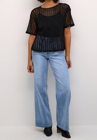 Top nero a maglia aperta con maniche corte abbinato a jeans a gamba larga blu chiaro e stivali neri alla caviglia. Il top presenta un collo rotondo e una vestibilità ampia.