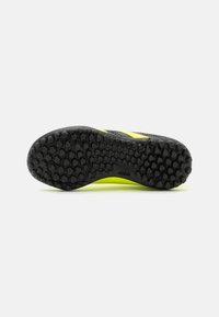 Suela de zapatilla deportiva negra con un patrón de tracción hexagonal, que presenta un acento amarillo brillante a lo largo de un lado. Material de goma duradera.