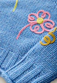 Lichtblauwe gebreide trui met een gestructureerd patroon, voorzien van roze en gele geborduurde bloemen- en swirlontwerpen.