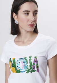 Camiseta de algodón blanca con un colorido gráfico texturizado de "ALOHA" con patrones florales y abstractos. Cuello redondo y mangas cortas.