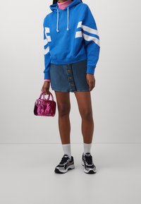 Blå huvtröja med vita ränder, denimkjol med knappar framtill, rosa glansig handväska och svarta sportskor med vita detaljer.