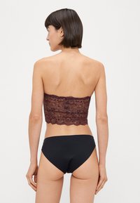 Bordový krajkový crop top so scalloped okrajmi, skombinovaný s čiernymi bikínami. Top má kvetinové vzory a je bez ramienok.