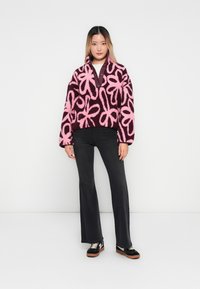 Fuzzy, pink and dark brown floral-patterned pullover made of plush fabric, paired with black flared pants and black sneakers with white accents.
