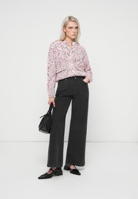 Růžová a bílá vzorovaná pletená blůza s límcem v kombinaci s kalhotami s vysokým pasem a širokými nohavicemi v černé barvě a černými špičatými botami. Součástí je černá kabelka.