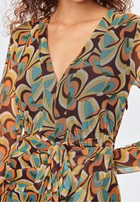 Bunt gemustertes Wickelkleid mit tiefem V-Ausschnitt, langen Ärmeln und einem Taillengürtel. Der Stoff hat abstrakte Wirbel in Braun, Orange, Blaugrün und Gelb.