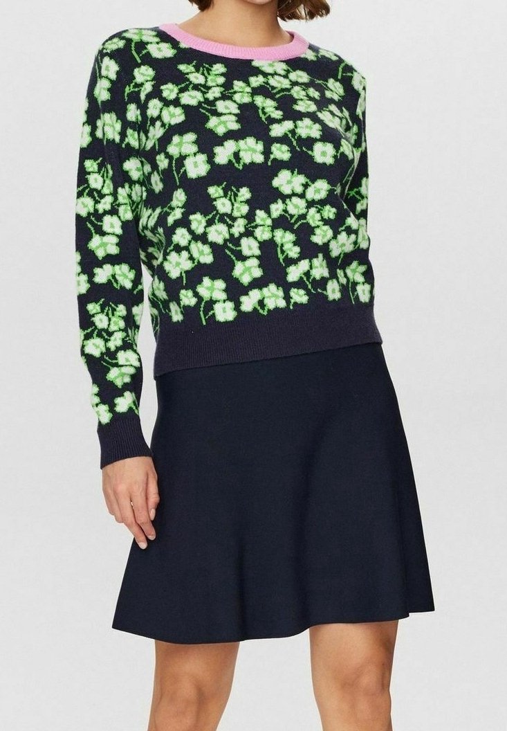 Dzianinowy sweter w kwiatowy wzór w kolorach zielonym i białym na granatowym tle. Posiada różowy ściągacz przy dekolcie i długie rękawy. W zestawie z granatową spódnicą.