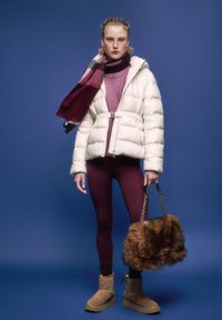 Biała kurtka puchowa z paskiem w talii, w połączeniu z bordowym golfem, dopasowanymi legginsami, brązową futrzaną torebką i beżowymi botkami za kostkę.