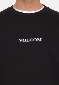 Schwarzer Pullover aus Baumwolle, mit Rundhalsausschnitt, mit weißem, gesticktem "VOLCOM"-Text auf der Vorderseite. Geschmeidige Textur, lässige Passform.