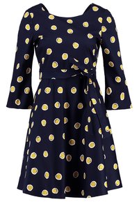 Robe bleu marine à pois jaunes et blancs, manches évasées trois-quarts, encolure ronde et ceinture nouée à la taille.