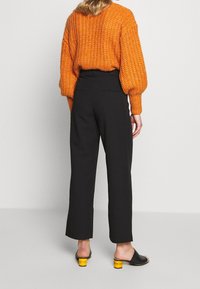 Oranje gebreide trui met pofmouwen, gecombineerd met zwarte wijde broek en zwarte muiltjes met gele blokhakken.