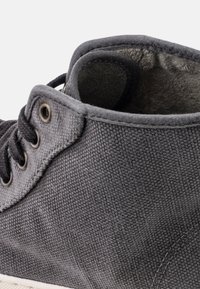 Zapatilla alta de lona gris con superficie texturizada, punta redonda, ojales metálicos y un interior suave. Suela de goma visible en la parte inferior.