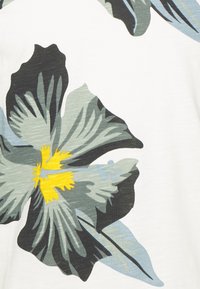 Blomstrete stoff med store, grønn-blå og svarte blomster med gule midtpunkter på hvit bakgrunn; glatt tekstur.