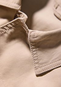 Collare in tessuto beige con una texture liscia, caratterizzato da cuciture visibili e un bordo arrotondato, che mette in risalto i dettagli del design del collare.