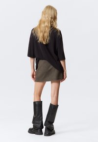 Pre veľkú čiernu tričko, mini sukňu z hnedého tweedu a vysoké čierne kožené čižmy so voľným dizajnom. Model zobrazený zozadu.