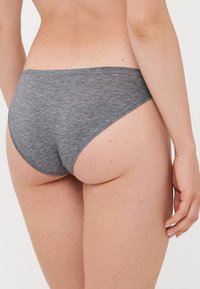 Woman wearing gray cotton underwear shown from the lower back to mid-thigh against a white background.
