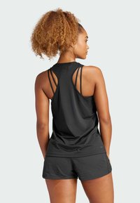 Zwart sporttopje met meerdere banden op de rug, gecombineerd met zwarte shorts met een subtiele textuur en een losse pasvorm. Glad materiaal, casual ontwerp.