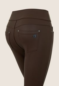 Pantaloni a vita alta marroni realizzati in un materiale elastico, con due tasche posteriori dotate di hardware argentato e un'etichetta logo sulla tasca destra.
