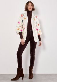 Cardigan crema lavorato a maglia con accenti floreali colorati, abbinato a jeans a vita alta marrone scuro e stivaletti alla caviglia in suede marroni.