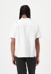 Short-sleeved white shirt with a textured fabric, straight fit, and a simple collar. Plain back view, no visible patterns or accents.