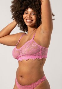 Roze kanten bralette en bijpassende thong met golvende randen. Doorzichtige textuur met bloemenpatronen en verstelbare bandjes. Verstelbare sluiting aan de achterkant.