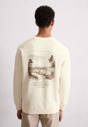 Cream-colored sweatshirt with a round neck and drop shoulder design. Features a brown graphic of a landscape and text on the back.