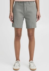 Pantalones cortos de mezcla de algodón gris con un corte recto, cierre de botón, bolsillos laterales y dobladillos enrollados. Combinados con zapatillas ligeras.