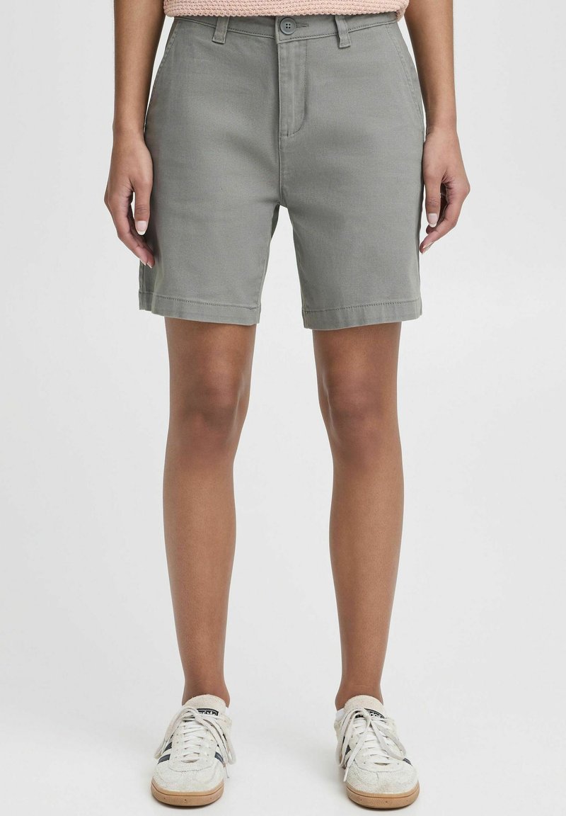 Pantalones cortos de mezcla de algodón gris con un corte recto, cierre de botón, bolsillos laterales y dobladillos enrollados. Combinados con zapatillas ligeras.