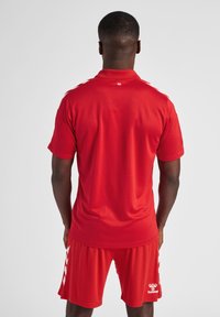 Rode sporttrui met korte mouwen, bijpassende rode shorts, voorzien van witte zijkanten en een logo op de zoom. Glad, lichtgewicht stof.