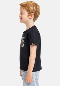 Camiseta de algodón negra con un diseño gráfico en colores verde brillante y púrpura en la parte delantera, mangas cortas y cuello redondo.