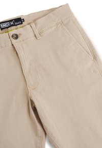 Pantalones de algodón beige con una textura suave, que cuentan con un cierre de botón, bolsillos laterales y un discreto detalle de logo en la cinturilla.