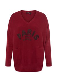 Roter V-Ausschnitt-Pullover mit langen Ärmeln, ausgestattet mit zwei Fronttaschen und einem schwarzen Pailletten-Textdruck: "PARIS MON AMOUR" in einem geschwungenen Design.