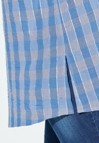 Tessuto a quadri blu e grigio con strisce argento, caratterizzato da una fessura sul lato. Superficie testurizzata con un aspetto leggero e tessuto.