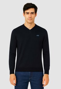 Maglione nero a collo a V realizzato in un tessuto morbido. Caratterizzato da maniche lunghe e polsini a coste, con un accento di logo azzurro sul petto.