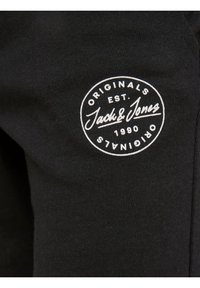 Tissu noir avec un logo circulaire blanc indiquant "Originals Est. Jack & Jones 1990 Originals" en haut à gauche.