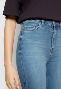 Jeans ajustados de mezclilla azul con cintura alta, desvanecimiento sutil y bolsillos cosidos; combinados con una camiseta negra de manga corta.