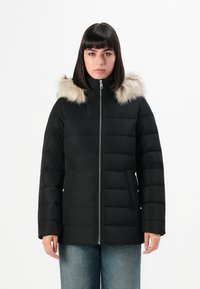 Giacca a vento nera con cappuccio foderato di pelliccia, dotata di zip frontale, design trapuntato e due tasche laterali. Texture liscia e isolamento caldo.