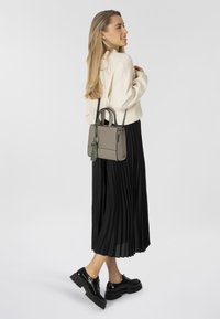 Borsa beige con manici e tracolla staccabile, caratterizzata da un nastro verde come accent. La gonna nera plissettata e le scarpe nere lucide completano l'outfit.