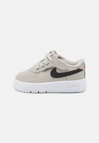Nike szürke velúr tornacipő fekete logóval, fehér talppal és fűzős dizájnnal. A lábujjnál perforációk találhatók a szellőzés érdekében.