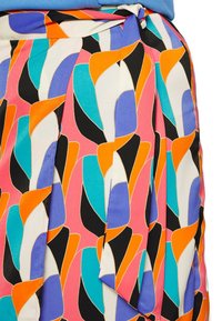 Jupe avec un motif géométrique abstrait coloré en orange, bleu, sarcelle, noir, violet et blanc, nouée à la taille avec un nœud.